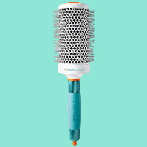 A MOROCCANOIL ceramic round brush with a white handle, black bristles, and an orange tip.