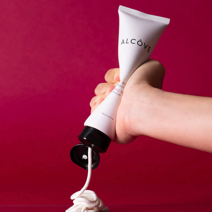 Hand holding a tube of Alcove cream against a red background